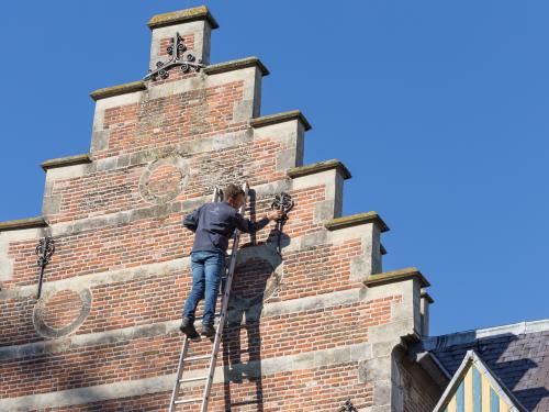 Monumentenwachter staat op ladder en inspecteert het monument